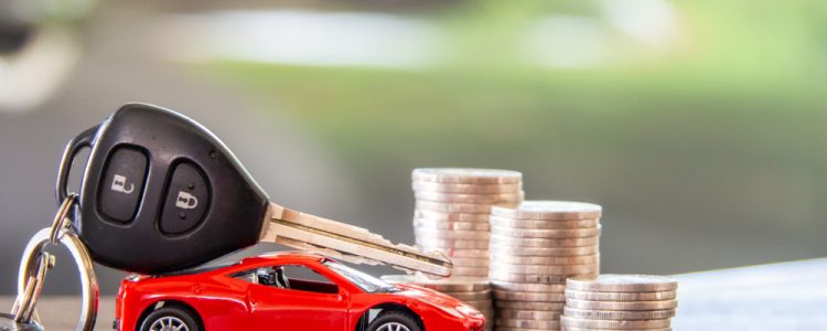 A toy red car with car keys resting on top, positioned next to several stacks of coins, symbolizing car expenses or financing