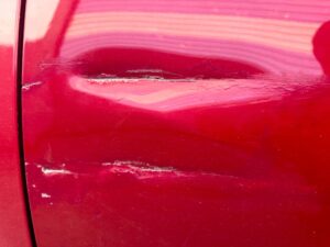 Close-up of a red car door with deep horizontal scratches and paint damage