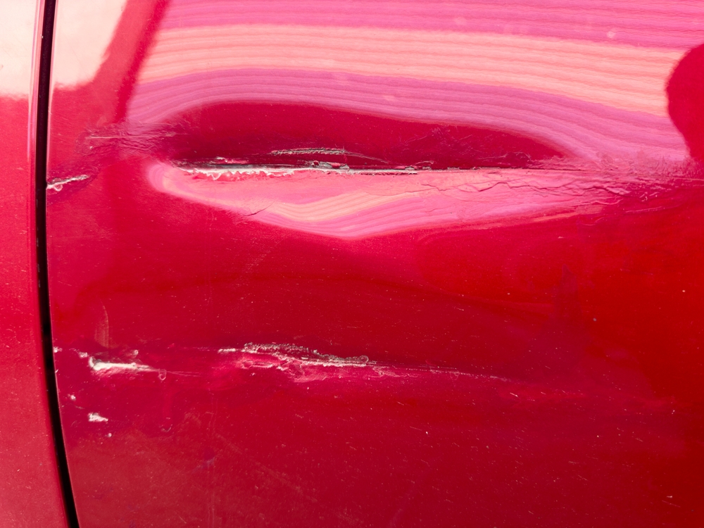 Close-up of a red car door with deep horizontal scratches and paint damage