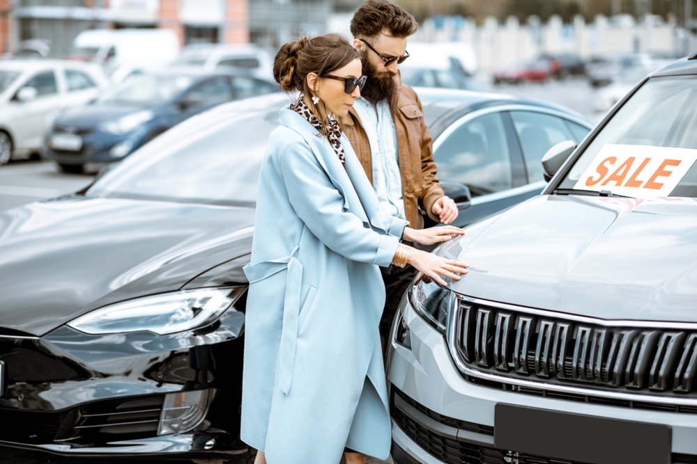Couple inspecting a gray SUV with a SALE sign on windshield at a car dealership lot
