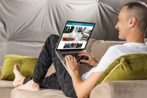 Man reclining on couch, smiling while browsing an auto sales website on a laptop