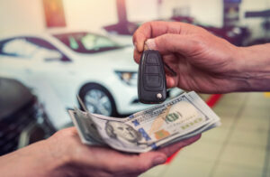 Person handing over car keys in exchange for a stack of hundred-dollar bills at a car dealership