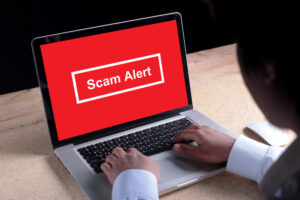 Person using a laptop displaying a red screen with the warning message “Scam Alert.”