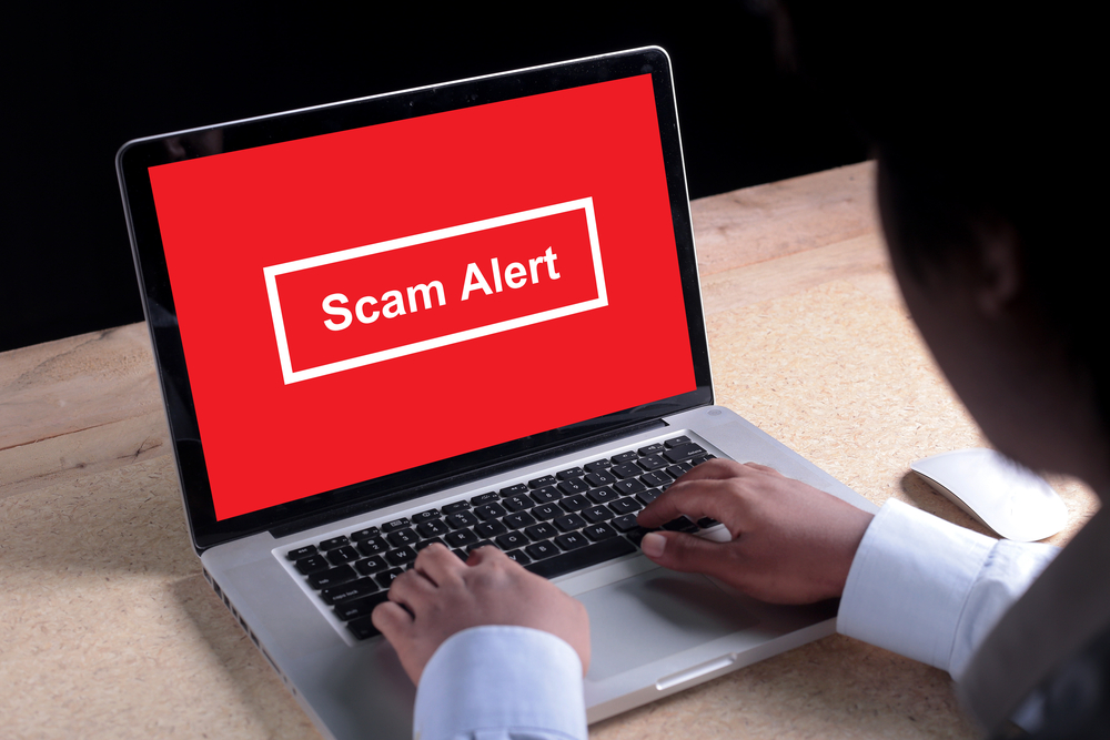 Person using a laptop displaying a red screen with the warning message “Scam Alert.”