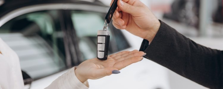 Close-up of a person handing car keys to another person, with a white car in the background