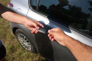 Two people exchanging car keys beside a silver car, symbolizing a car handover or sale