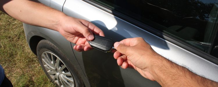 Two people exchanging car keys beside a silver car, symbolizing a car handover or sale